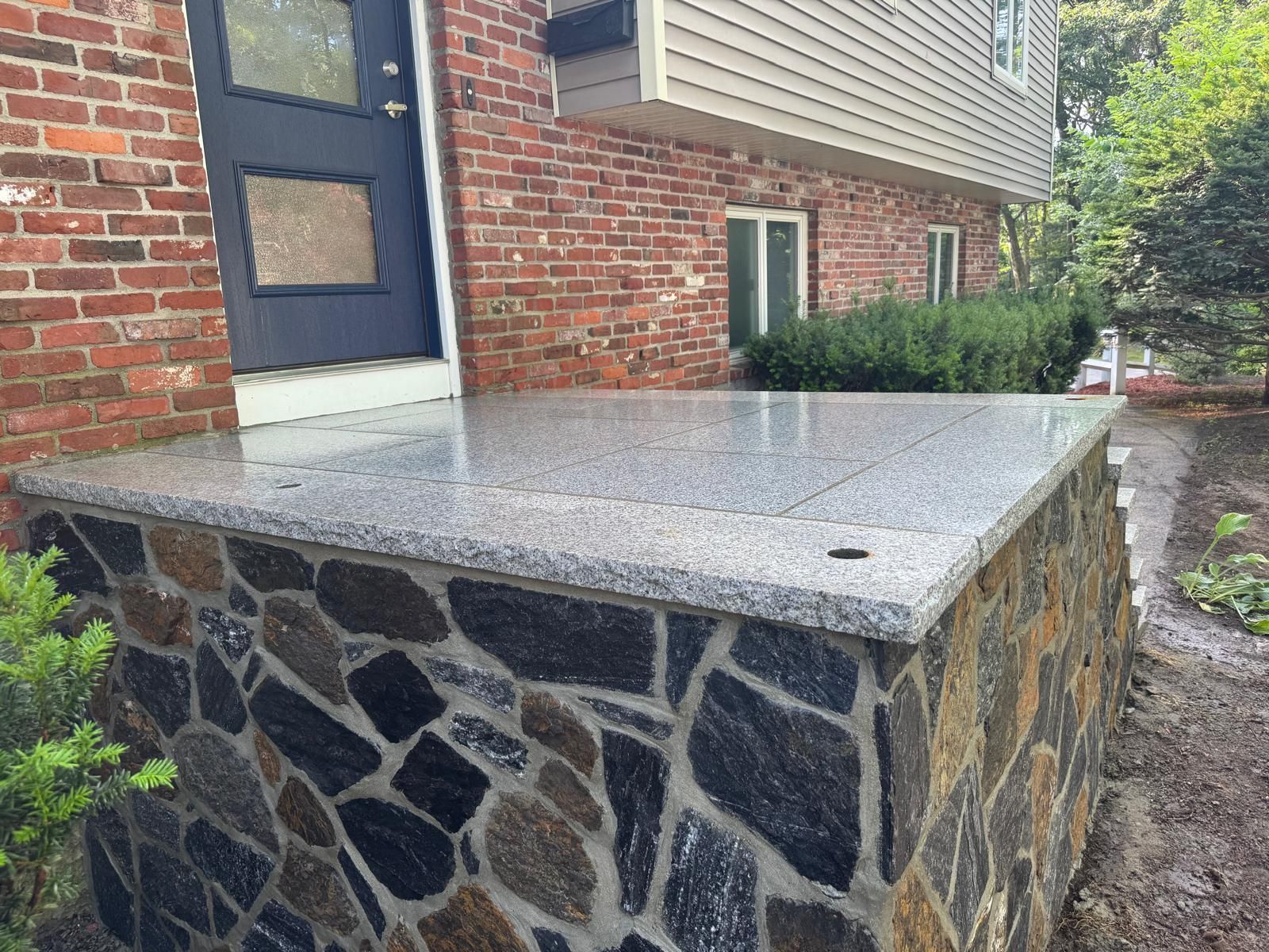 Stone-clad porch with a concrete top beside a brick house entrance