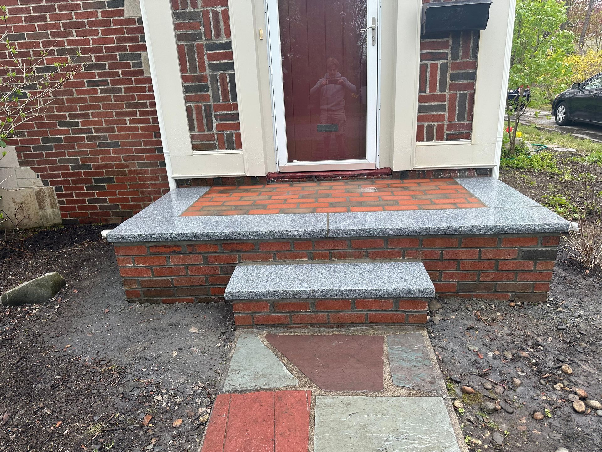 Brick front stoop with two concrete steps leading to a red door and tiled landing.
