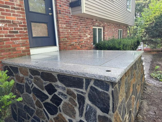 Stone-front porch with concrete steps beside a brick house and blue door