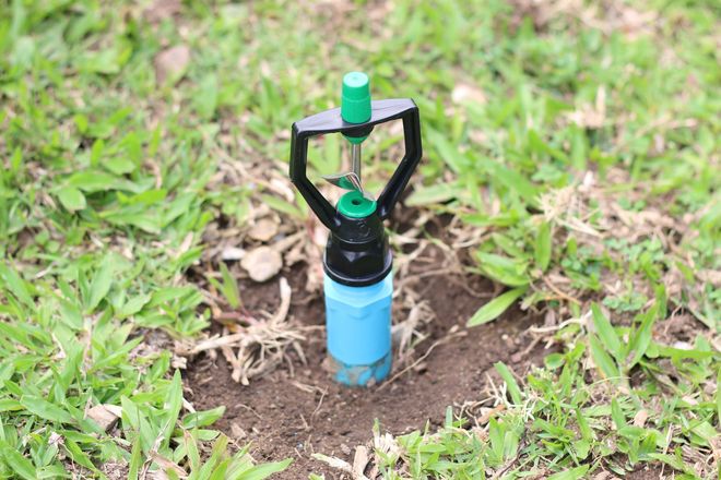 A lawn sprinkler with a black frame and blue base in a patch of green grass.