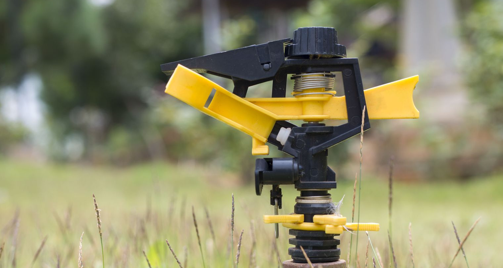 Yellow and black sprinkler in a grassy yard, blurred background.