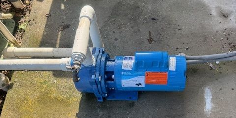 Blue water pump with white pipes on a concrete surface.