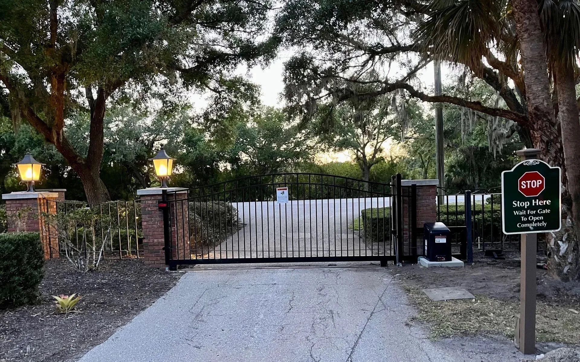 A gated entrance to a private driveway, lined with brick pillars, outdoor lanterns, and a red stop sign on a post.