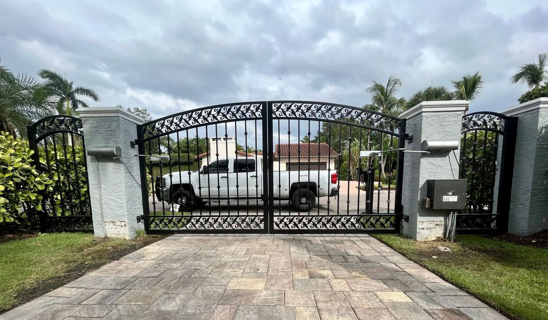A white truck parked behind a closed, arched black metal gate situated between two gray stone pillars.