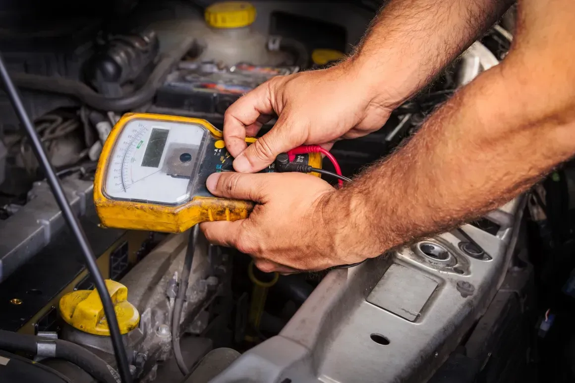 Hands using a multimeter to test a car engine. Yellow device with red and black leads.