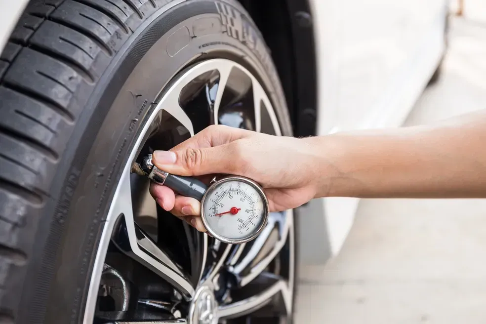 Person checks tire pressure with a gauge on a car tire.