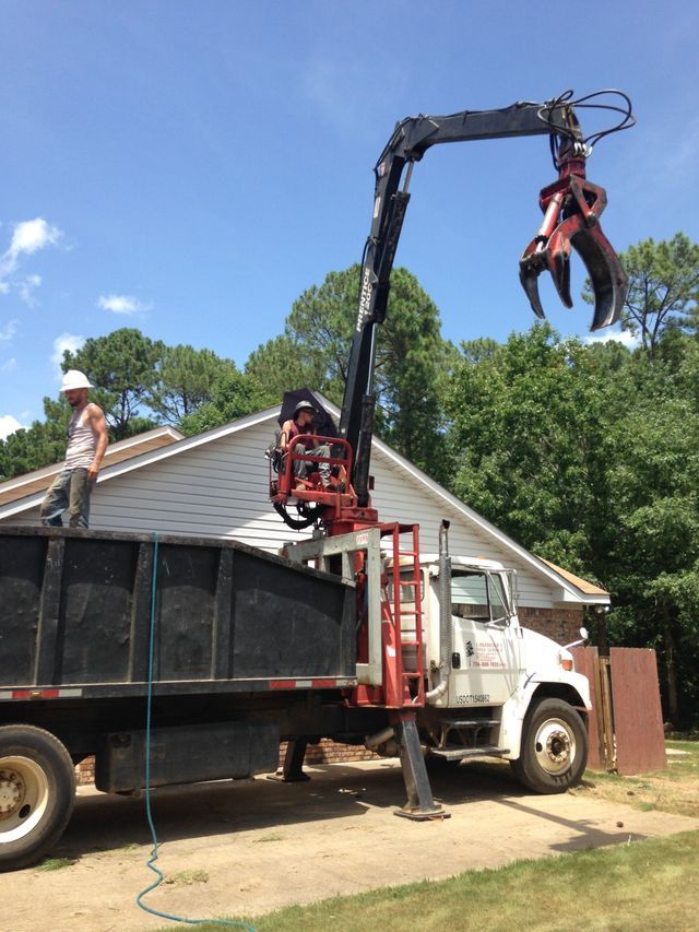 A dump truck with a crane attached to it is parked in front of a house.