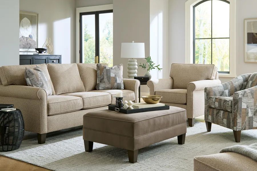 Bright living room with beige sofa, ottoman, armchair, and large windows with sheer curtains.