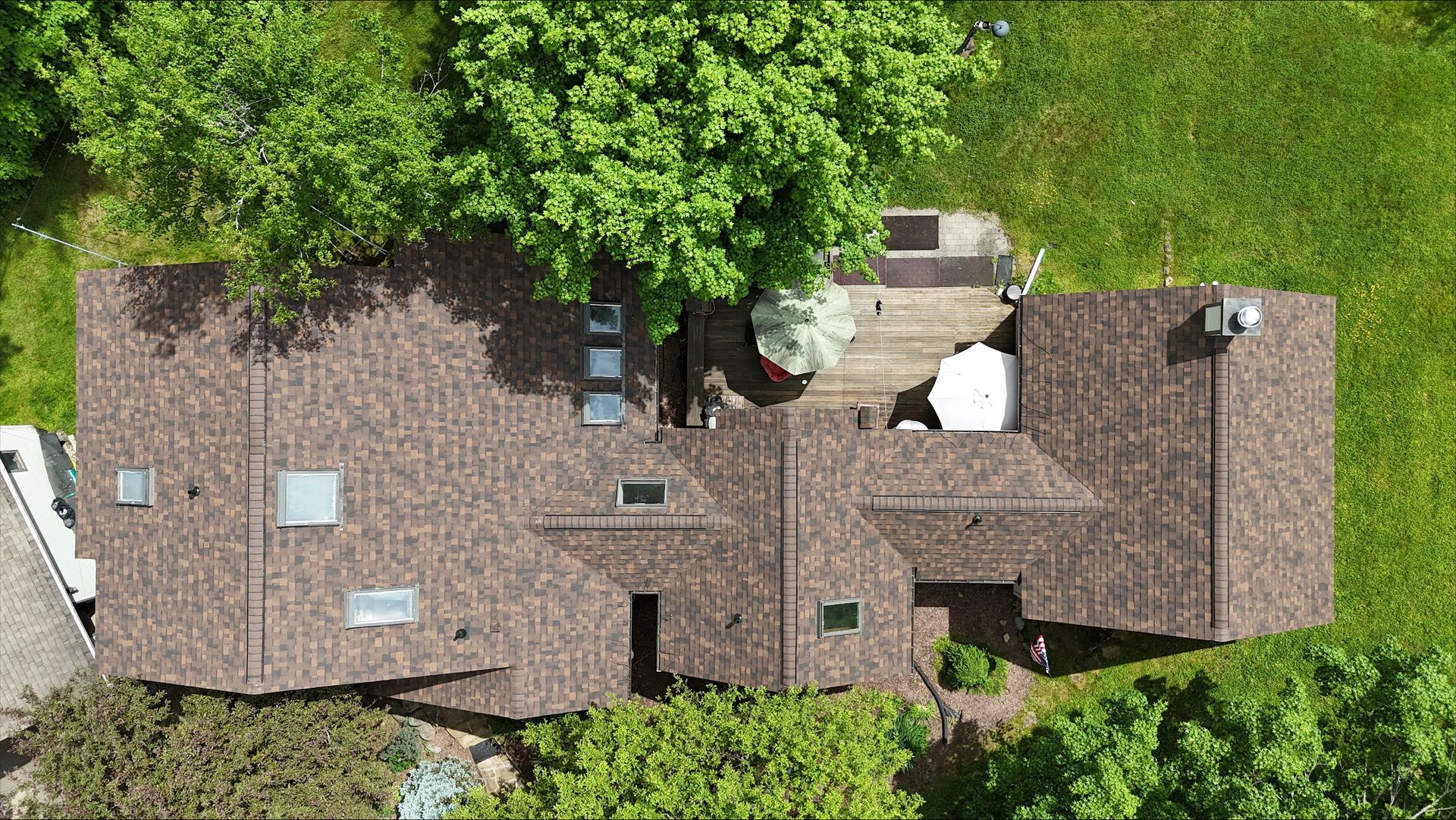 An aerial view of a house with a roof and a deck surrounded by trees.