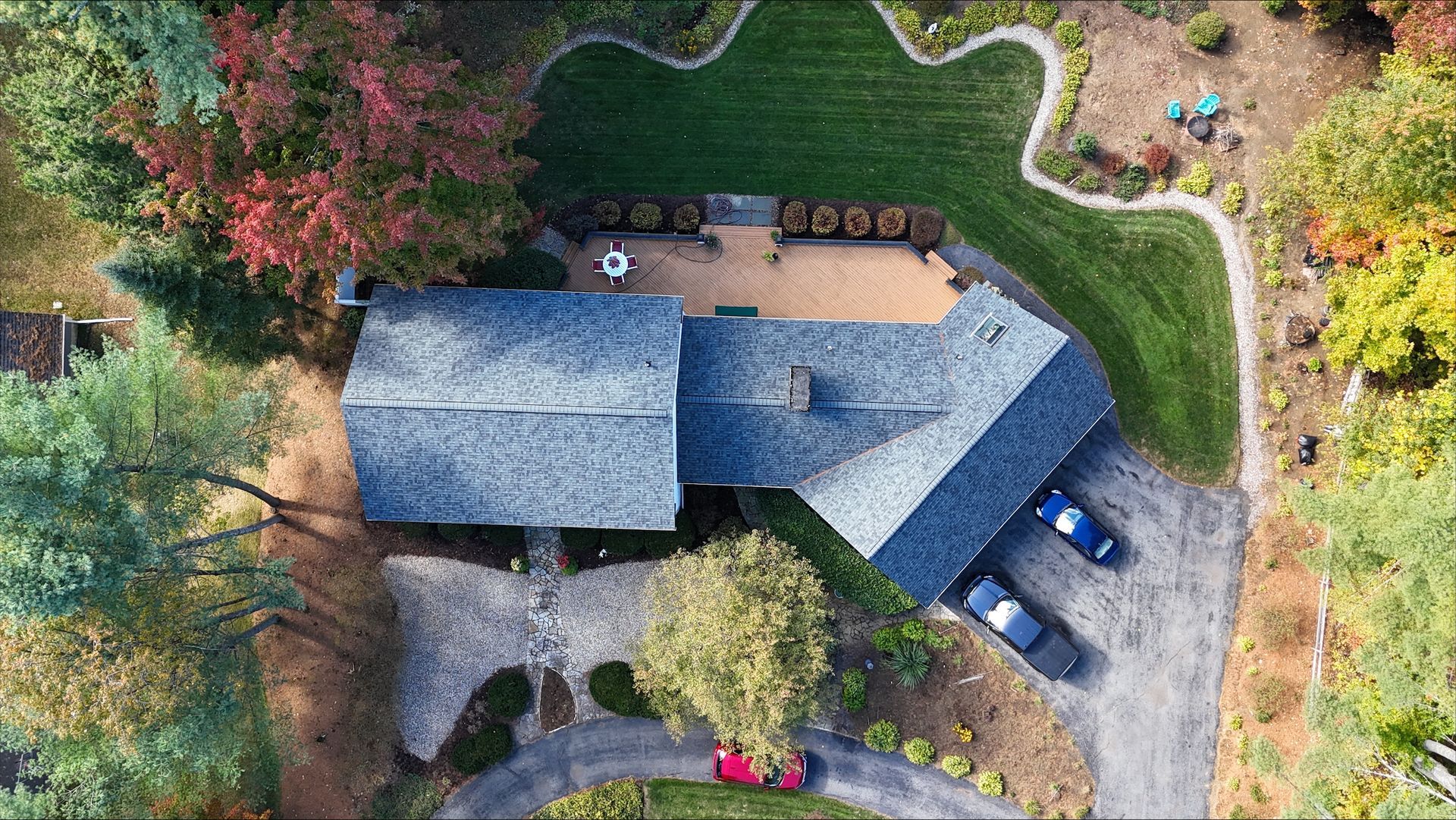 An aerial view of a house with cars parked in front of it surrounded by trees.
