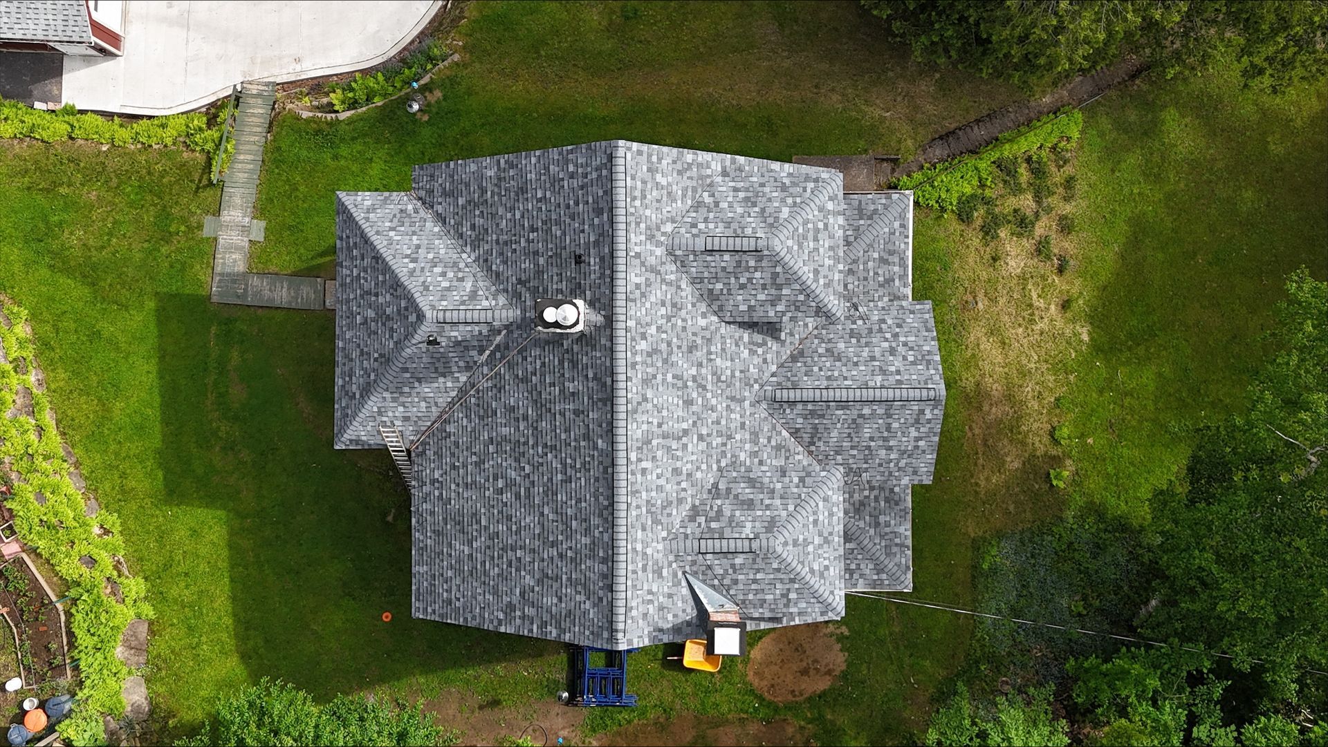 An aerial view of a house with a roof in the middle of a lush green field.