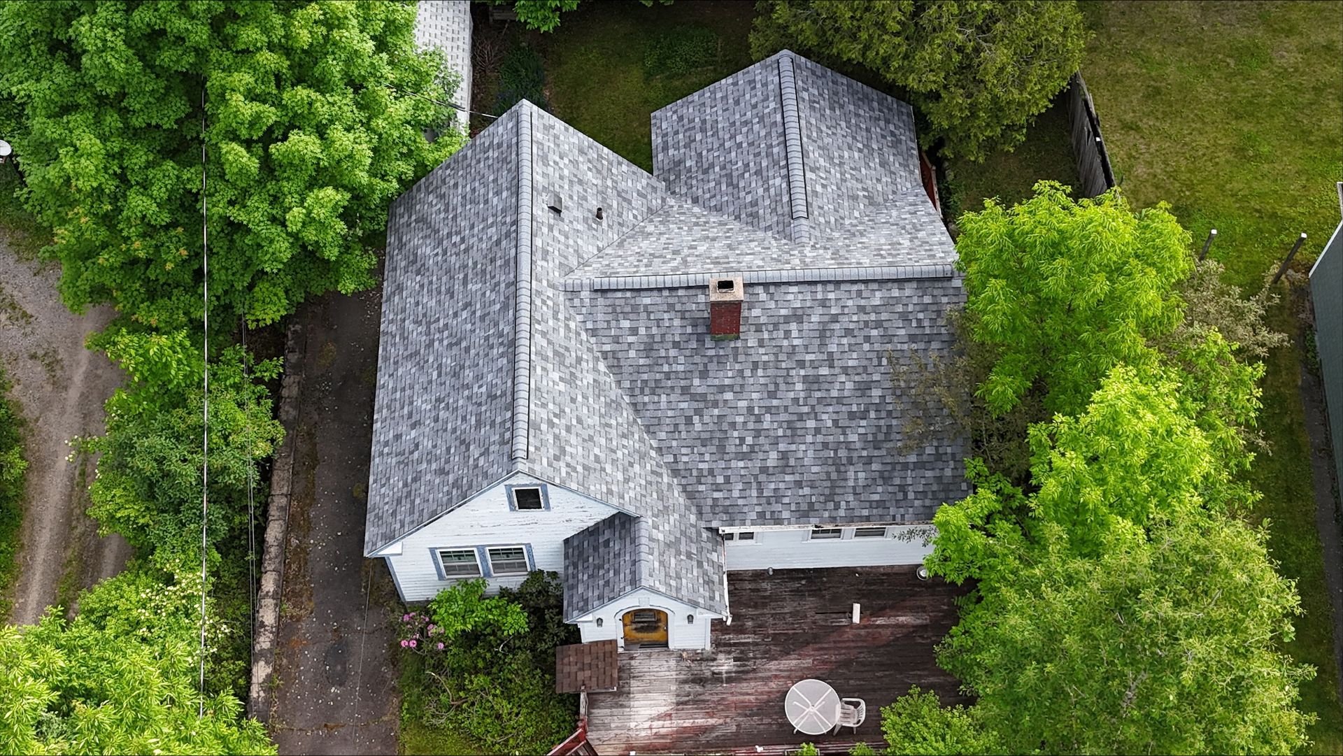 An aerial view of a house with a roof that is surrounded by trees.