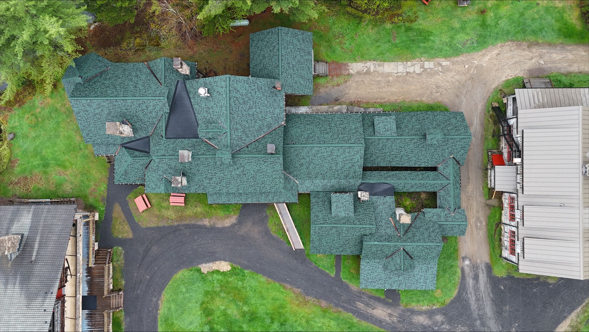 An aerial view of a large house with green roofs surrounded by trees.