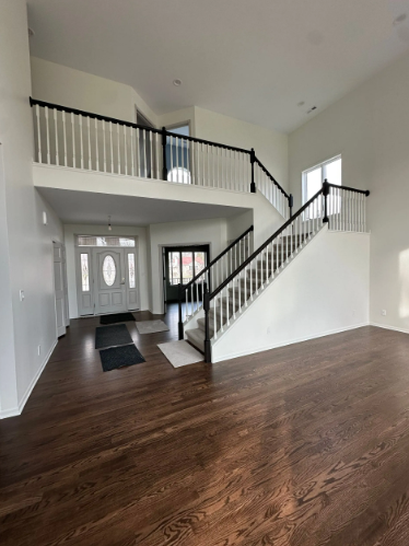 Interior view of a house with dark wood floors, white walls, and a staircase with black and white railing.