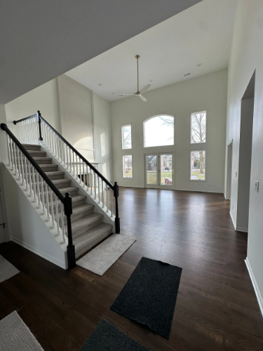 Spacious entry with staircase and tall windows, dark wood floor, and white walls.