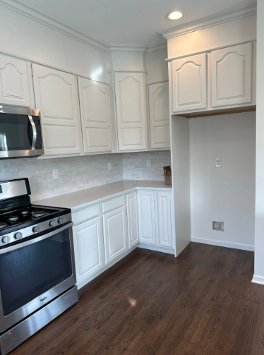 White kitchen with stainless steel appliances, white cabinets, and dark wood floors.