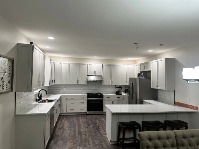 U-shaped kitchen with light gray cabinets, white countertops, stainless steel appliances, and dark wood-look flooring.