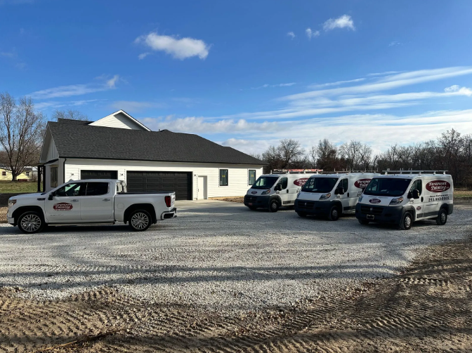 White service vehicles parked in front of a modern house on a gravel lot under a blue sky.
