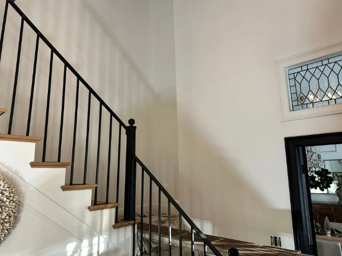Staircase with black railing and light-colored steps against a white wall; decorative window visible.