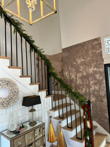Staircase decorated for the holidays with garland, ornaments, and festive wallpaper.