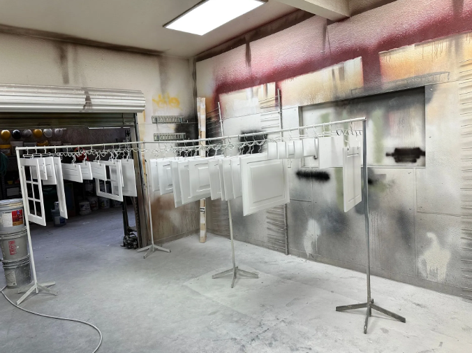 Spray paint booth with freshly painted white window frames and panels hanging to dry.