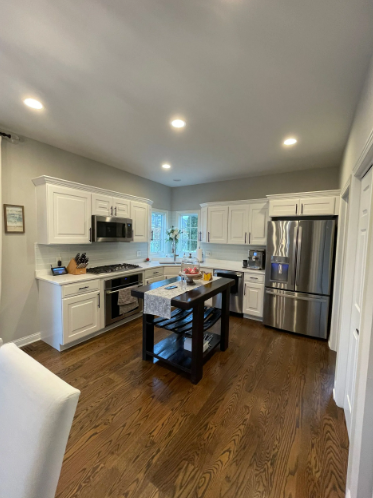 White kitchen with stainless steel appliances, dark wood floors, and black island.