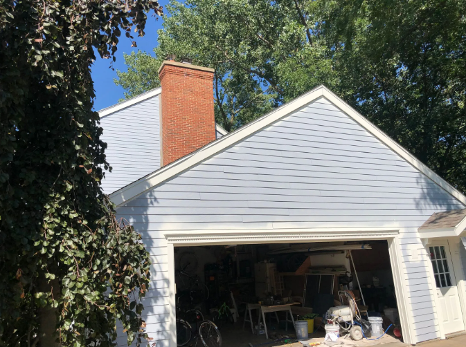 Blue house with a brick chimney, garage door open, and greenery in the foreground.
