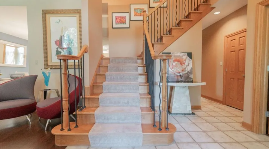 Foyer with staircase, artwork, and tile floor. Neutral color palette with wood and carpet.