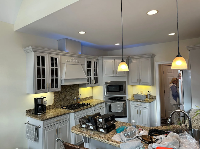 Kitchen with gray cabinets, granite countertops, and two pendant lights. A person is visible in the doorway.