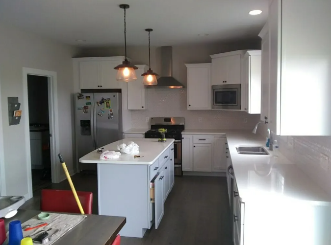 Modern kitchen with white cabinets, gray island, stainless steel appliances, and pendant lights.