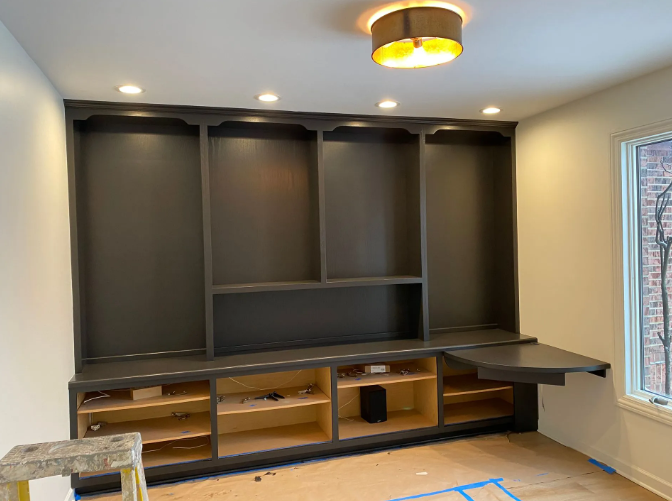 Built-in dark gray shelving unit with open cabinets and a pull-down desk. Recessed lighting in a room with a window.