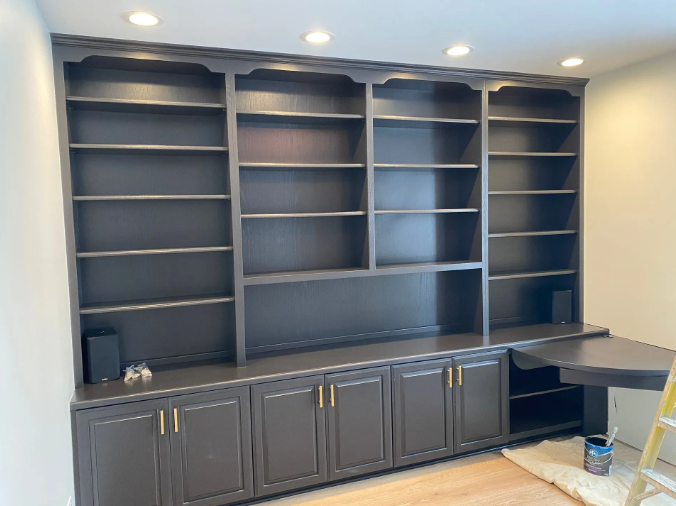 Built-in dark gray bookshelf with desk, gold hardware, and recessed lighting.
