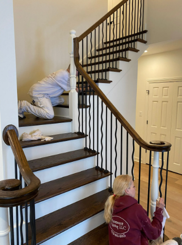 Two people painting a wooden staircase with white and dark brown accents.