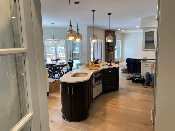 Kitchen island with microwave and sink, black cabinets, light wood floor, open to dining area.