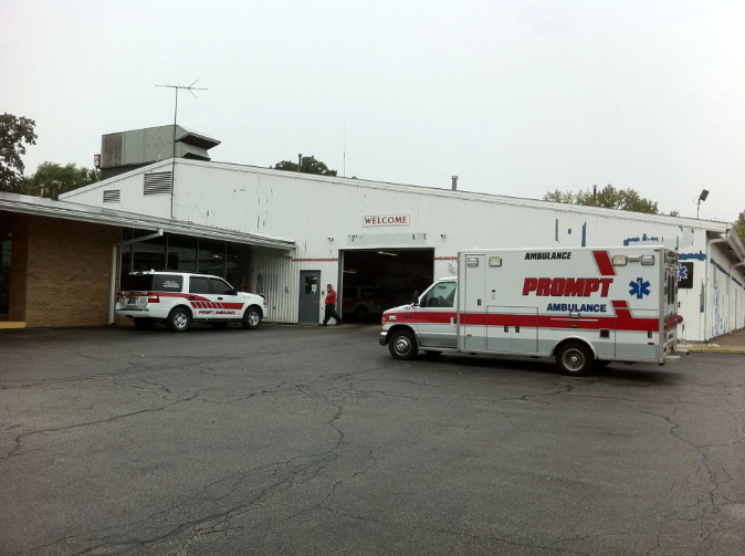 Ambulance and SUV parked outside a white building with the word 