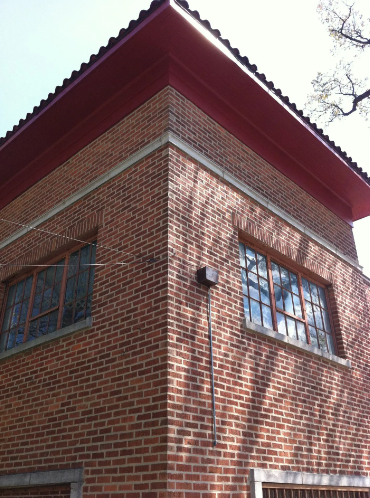 Corner of a brick building with windows, red roof, and shadows.