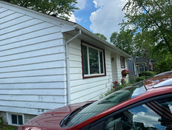 White house with red trim, gutter, and a red car parked nearby.