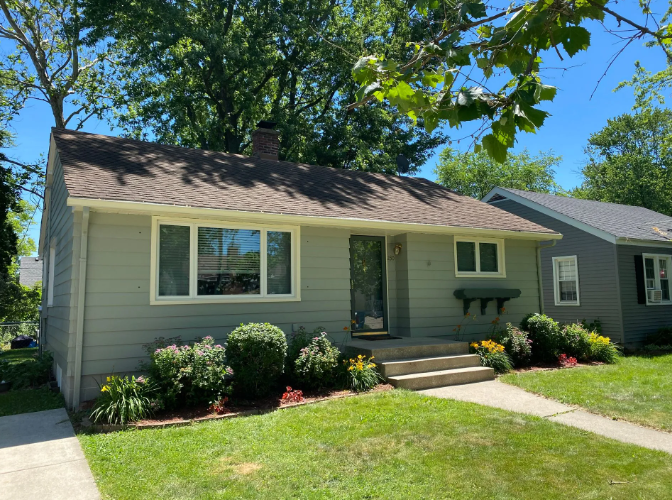 A light green, one-story house with white trim, a small front yard, and a concrete walkway.