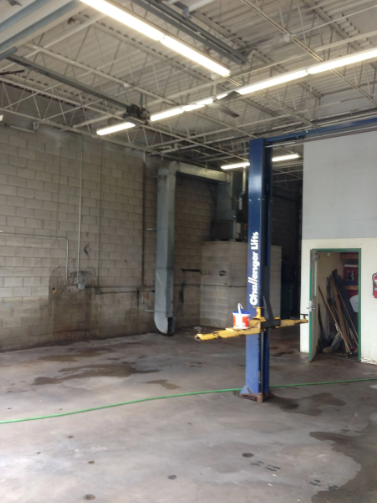 Interior of an auto repair shop with a vehicle lift; concrete floor, brick walls, fluorescent lights.