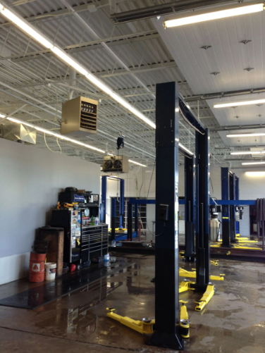Interior of an auto repair shop with vehicle lifts, tools, and a ceiling-mounted heater.