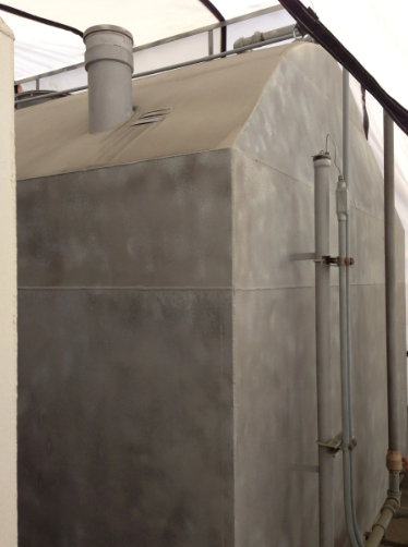 Gray, box-shaped industrial tank with a chimney. Pipe and other fittings on the side, under a white awning.