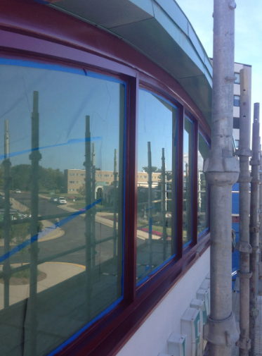 Curved building exterior with red-framed windows, blue tape, and scaffolding.