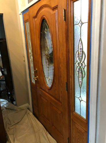 Wooden front door with oval glass and sidelights, taped off for painting.