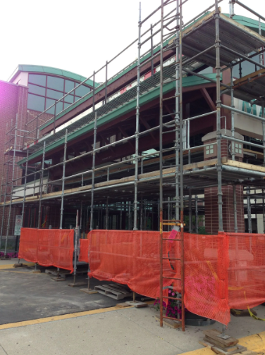 Building under construction, scaffolding wraps the exterior. Orange safety fencing lines the perimeter.