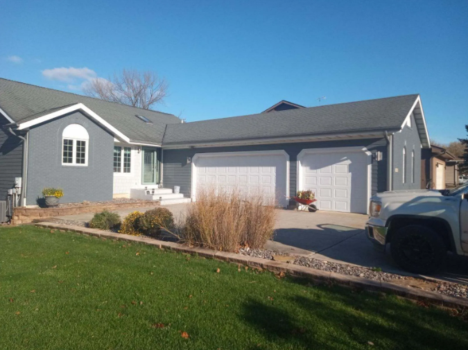 A two-story gray house with white garage doors and a green lawn on a sunny day.