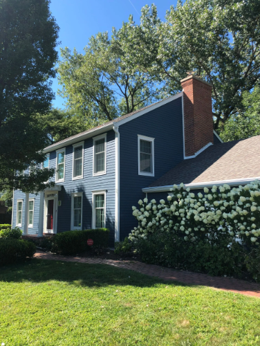 Two-story blue house with a brick chimney and green lawn, under a bright blue sky.