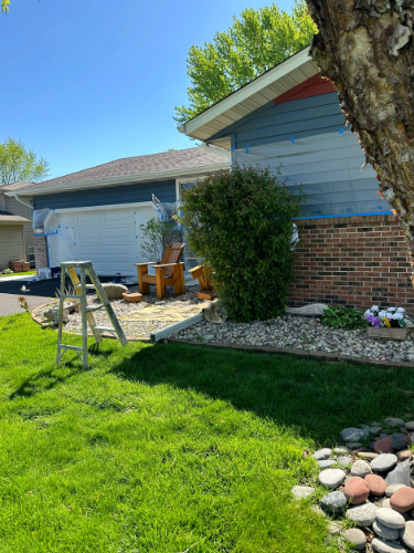 House exterior with blue siding, brick, and a white garage. A ladder and landscaping are in the yard.