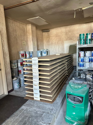 Interior shot of storage space with stacked wood panels, paint cans, and a green cleaning machine.