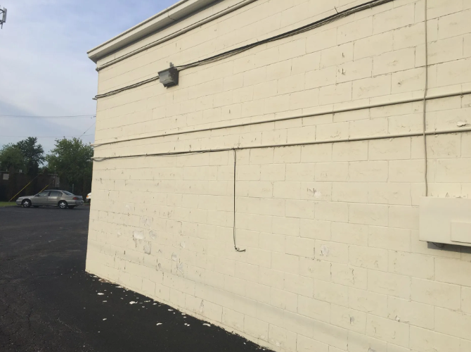 Cream-colored building exterior, gray asphalt parking lot, gray car in the background, overcast sky.