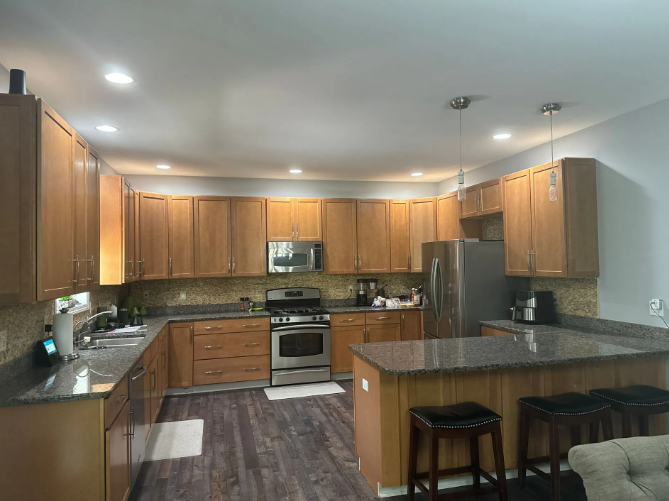 A kitchen with wooden cabinets, stainless steel appliances, dark countertops, and a center island with stools.